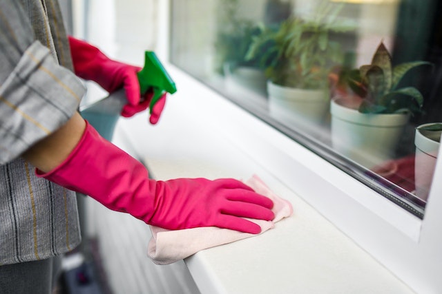 Person wearing pink gloves spraying down a windowsill